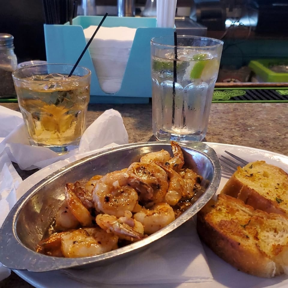 Sautéed shrimp with garlic bread, iced drinks, and condiments served at a restaurant bar.