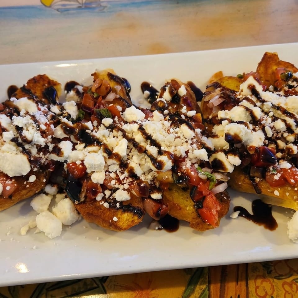 Platter of toasted bread topped with diced tomatoes, onions, crumbled cheese, and balsamic glaze.